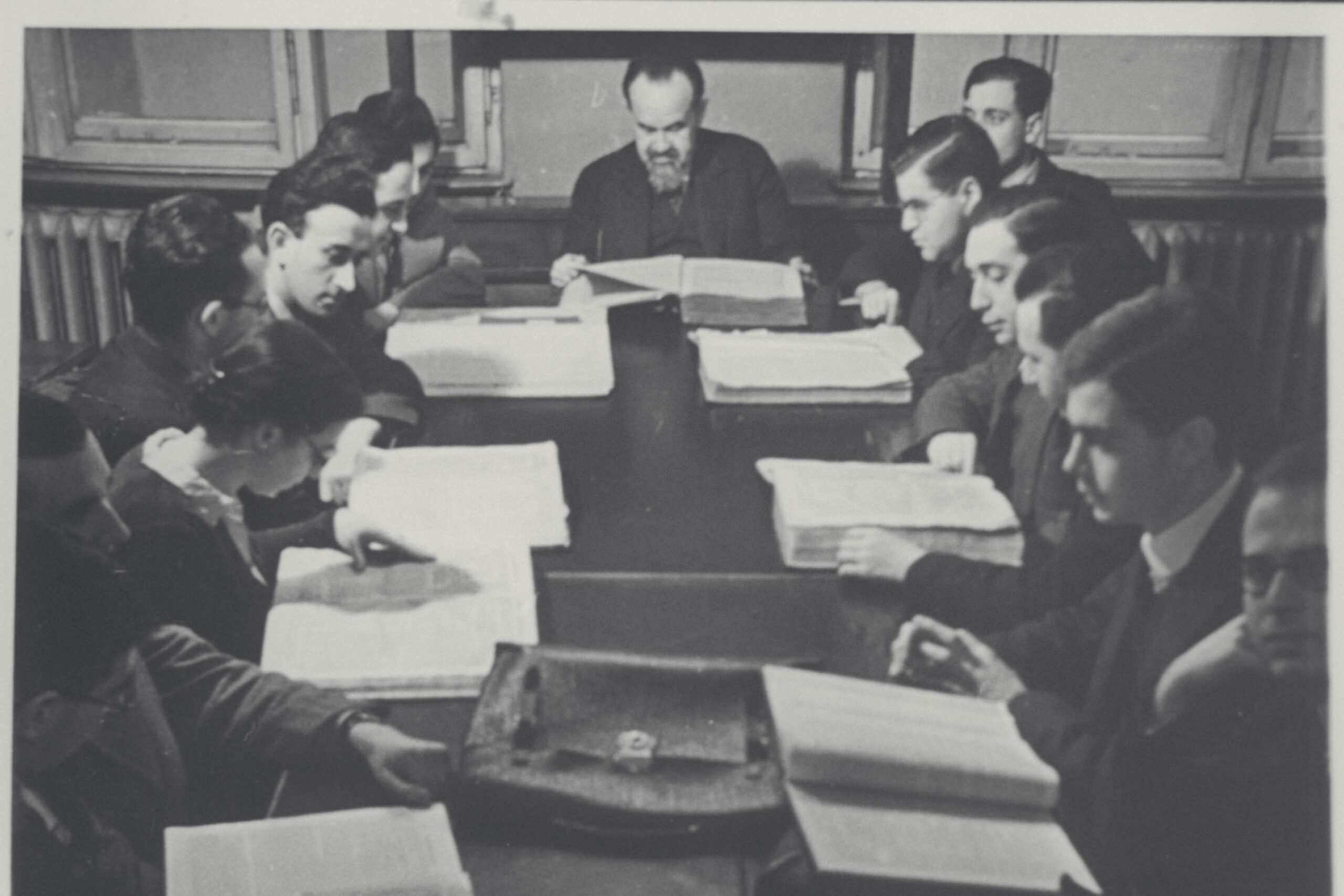Isamar Elbogen with students – Lehranstalt für die Wissenschaft des Judentums, Berlin People are seated around a long rectangular table. Ismar Elbogen is seated at the end of the table. There are papers on the table in front of the people.